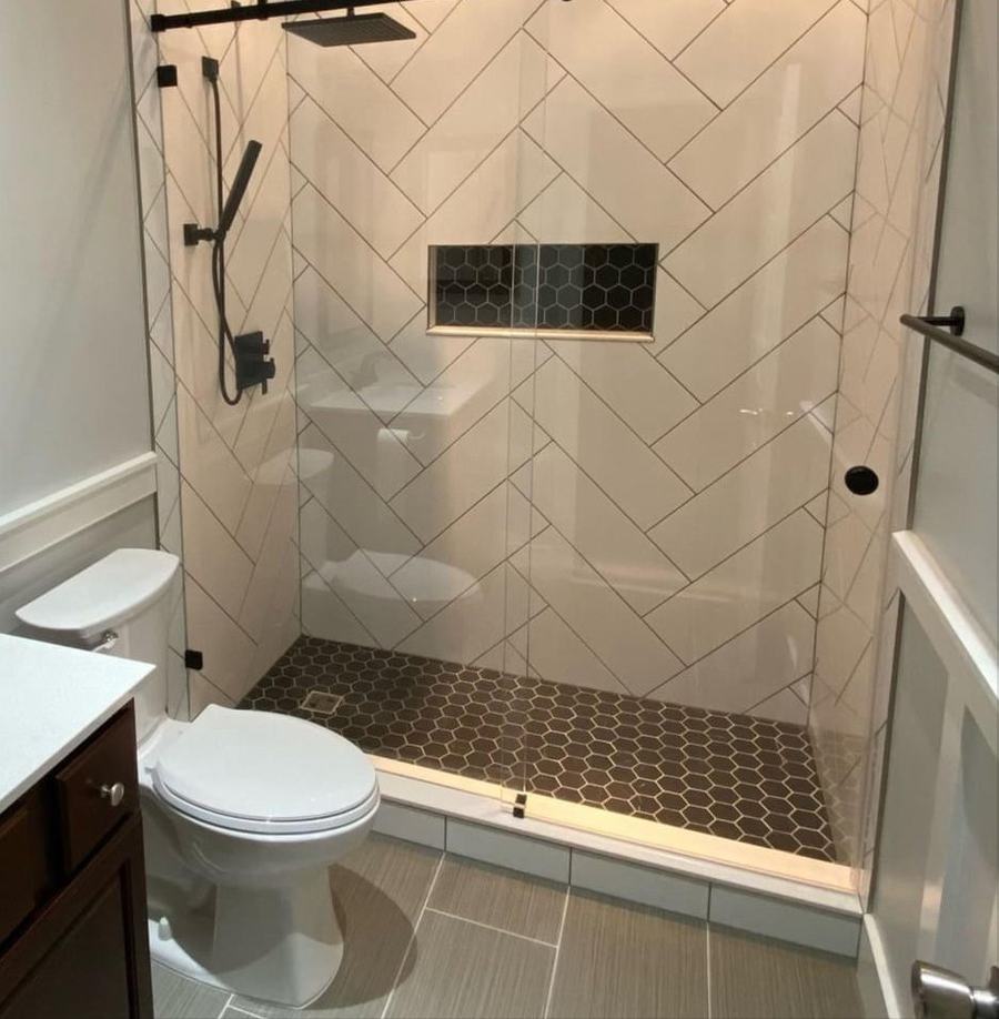 Walk-in shower with white rectangular tile set in a herringbone pattern, a recessed niche and black hexagon tile floor
