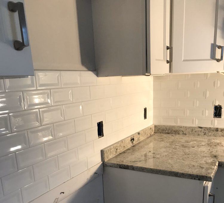 Kitchen corner with white beveled subway tile backsplash above a granite countertop and grey cabinets