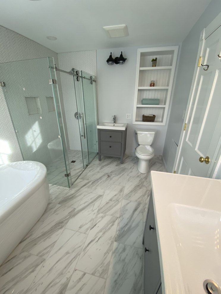 Bright bathroom with marble-look porcelain floor, sliding-door glass shower with herringbone wall tile and a freestanding tub