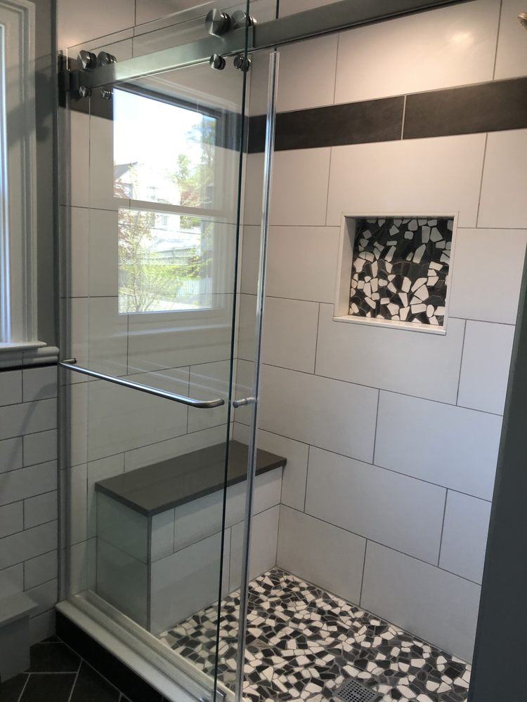 Shower with large white wall tile, charcoal accent band, built-in bench and black-and-white pebble mosaic niche and floor